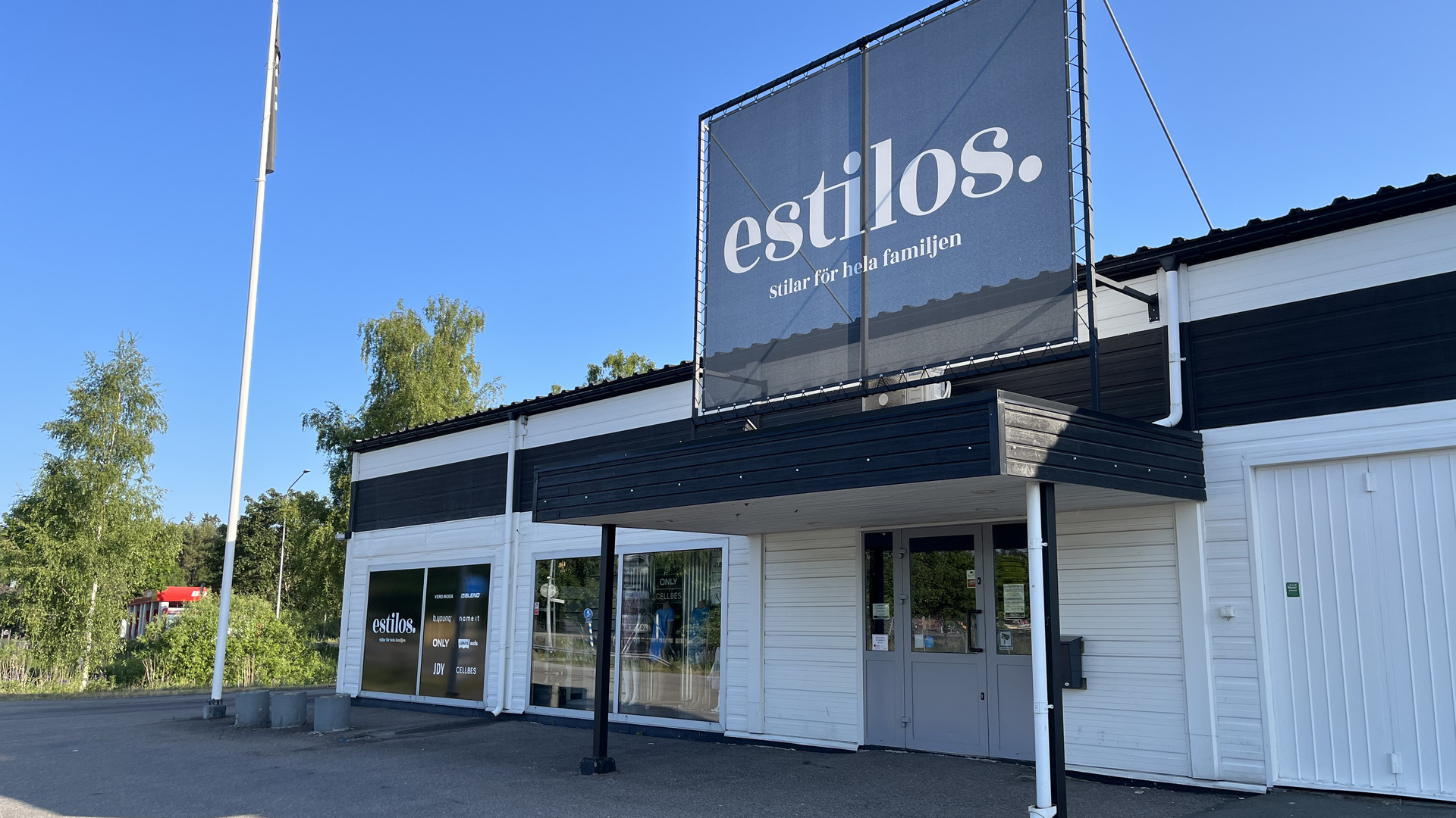 Vit butiksbyggnad med stor skylt "Estilos"