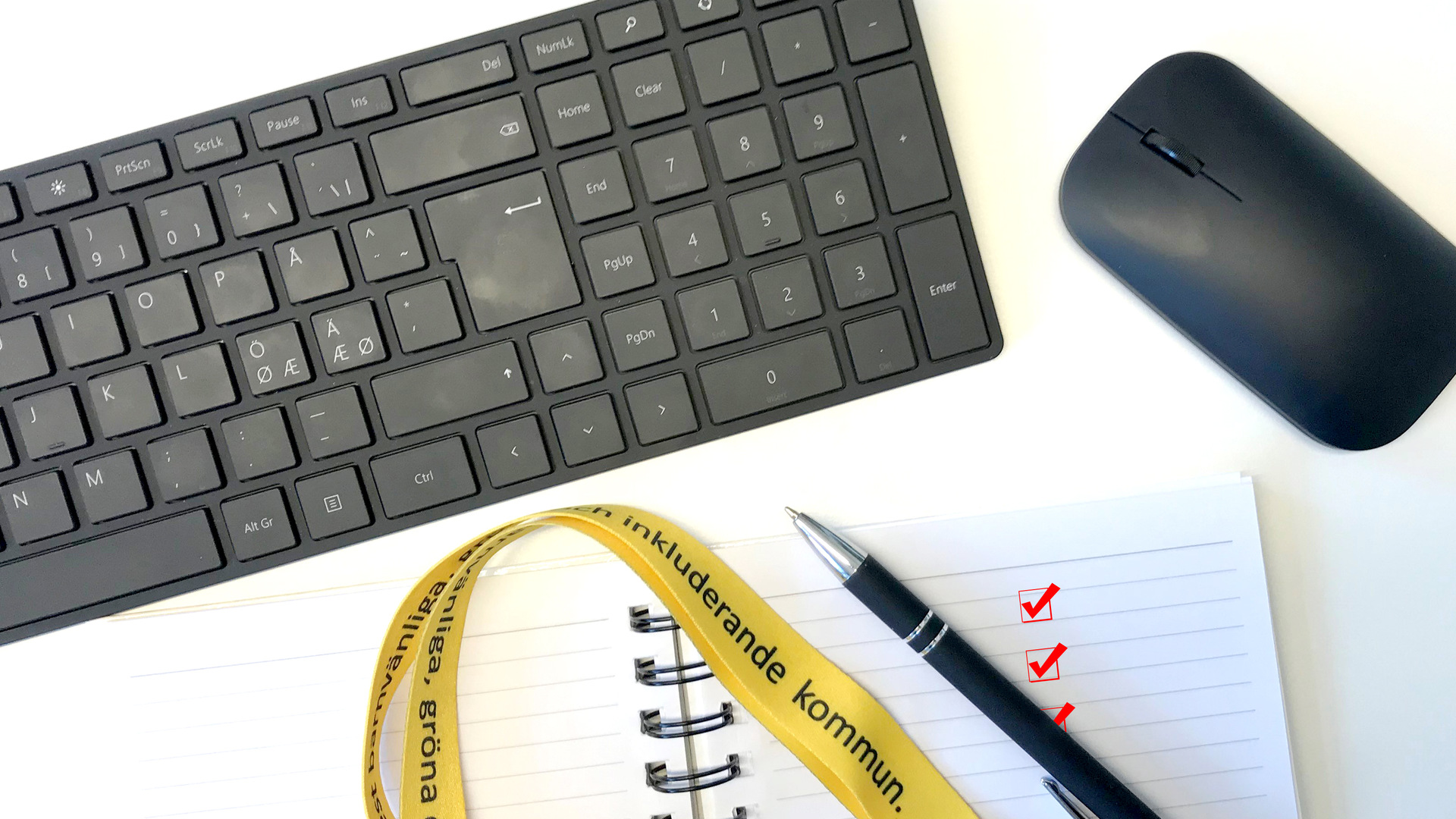 Ett tangentbord, en mus och ett skrivblock med en penna och ett nyckelband över
