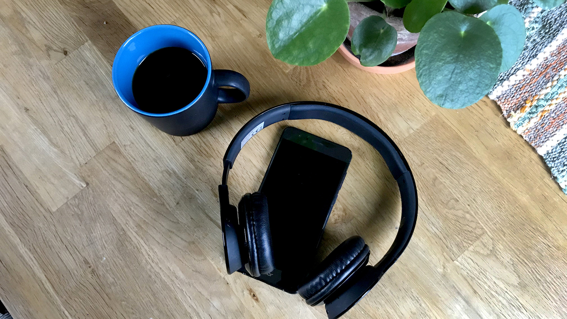 En blå kaffekopp och en svart mobiltelefon och hörlurar
